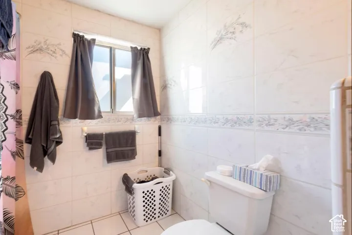 White ceramic tile flooring, white ceramic wall tiling, and a window with a white frame