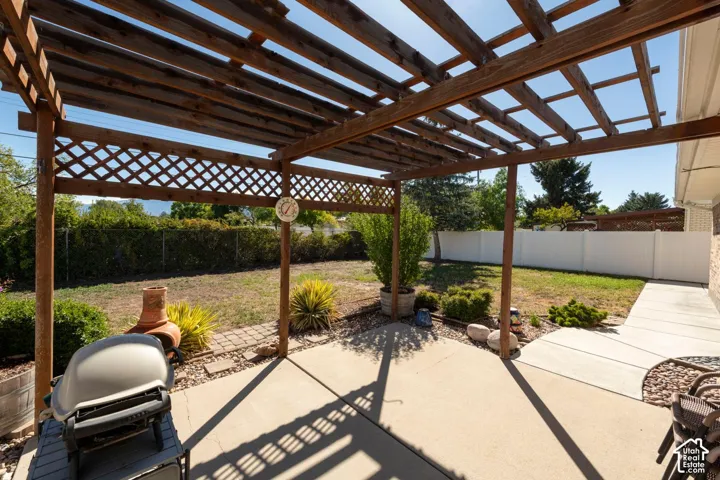 Wood pergola with lattice detailing, concrete patio, and fenced backyard with mature landscaping