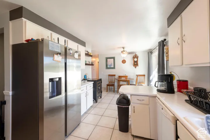 Stainless steel refrigerator, white cabinetry, white countertops, tile flooring, and integrated ceiling fan