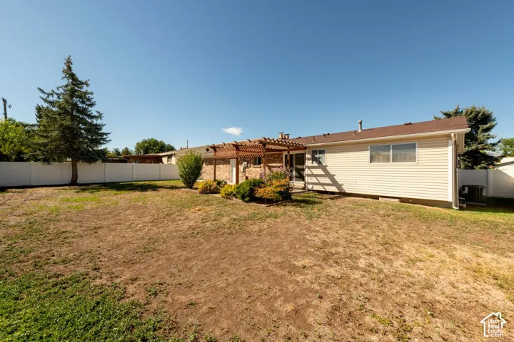 Expansive rear yard featuring a privacy fence, mature trees, and a pergola-covered patio area