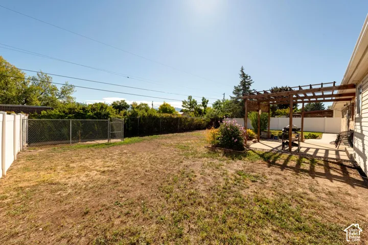 Expansive backyard featuring a concrete patio with a wooden pergola, privacy fencing, and mature landscaping
