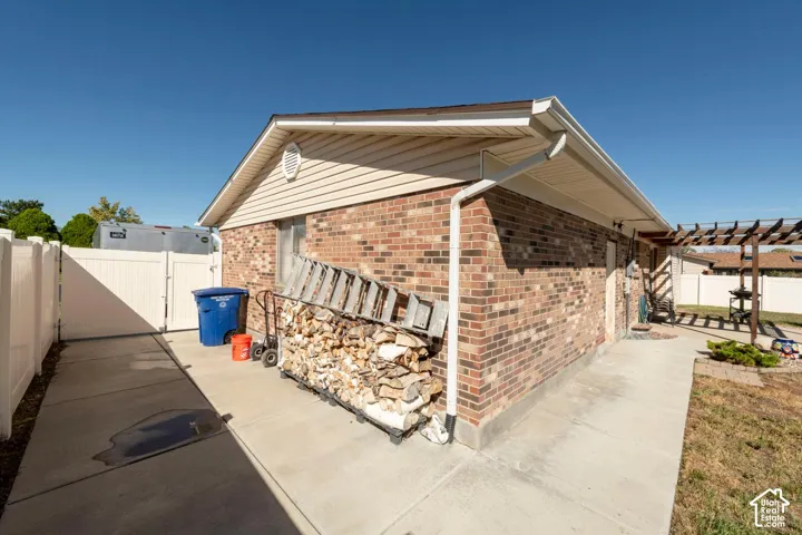 Brick exterior with horizontal siding accent, white vinyl fencing, concrete walkway, and a wooden pergola