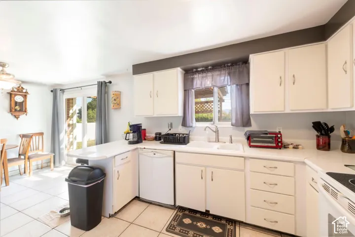White cabinetry with modern pulls, white countertop surfaces, and a double basin sink with a chrome faucet