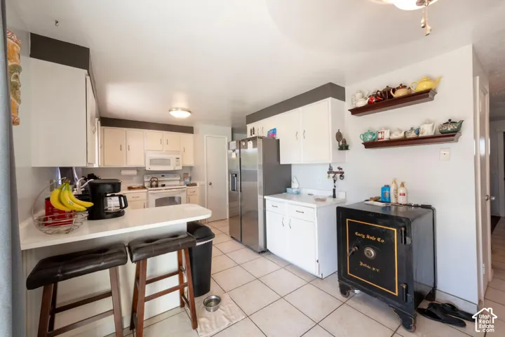 White cabinetry, stainless steel refrigerator, white countertops, tile flooring, and integrated breakfast bar