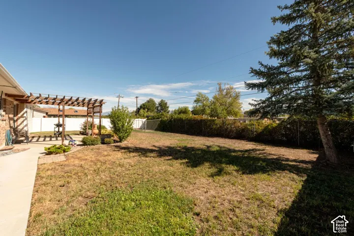 Expansive yard space featuring a concrete patio, wooden pergola, established shrubbery, and mature trees