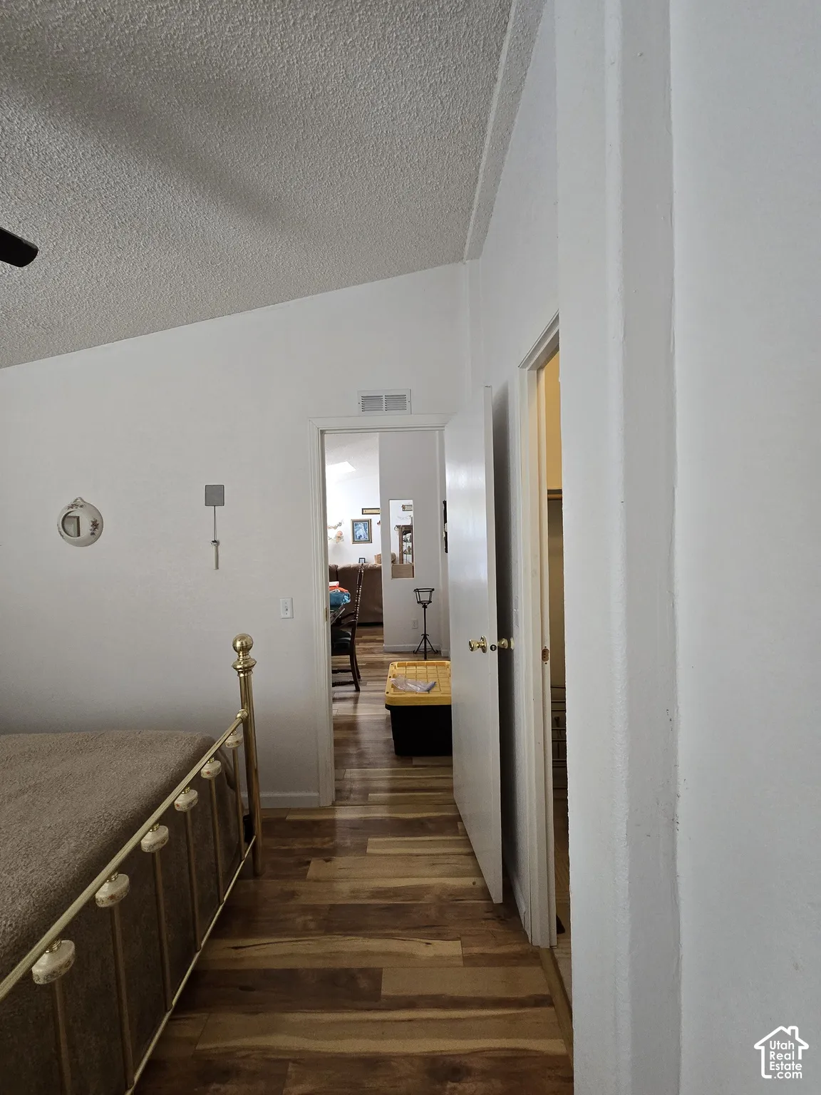 Vaulted ceiling with textured finish, wood-finish flooring, and white walls