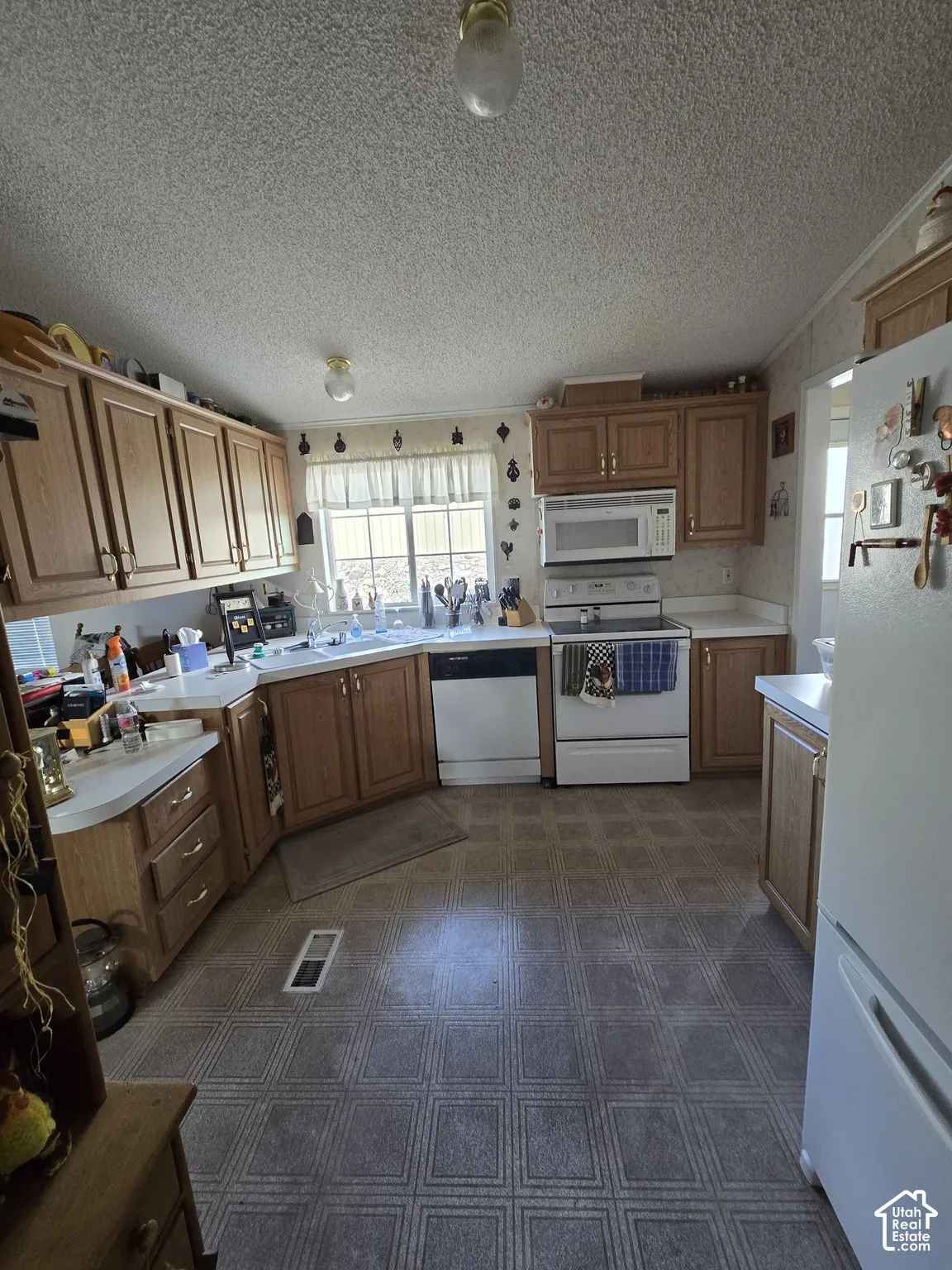 Kitchen featuring wood-finish cabinetry, patterned vinyl flooring, a double basin sink, and white appliances