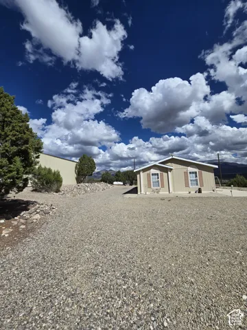 Gravel driveway with a single-story structure featuring tan siding and brown window shutters