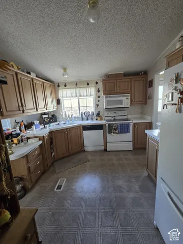 Kitchen featuring wood-finish cabinetry, patterned vinyl flooring, a double basin sink, and white appliances