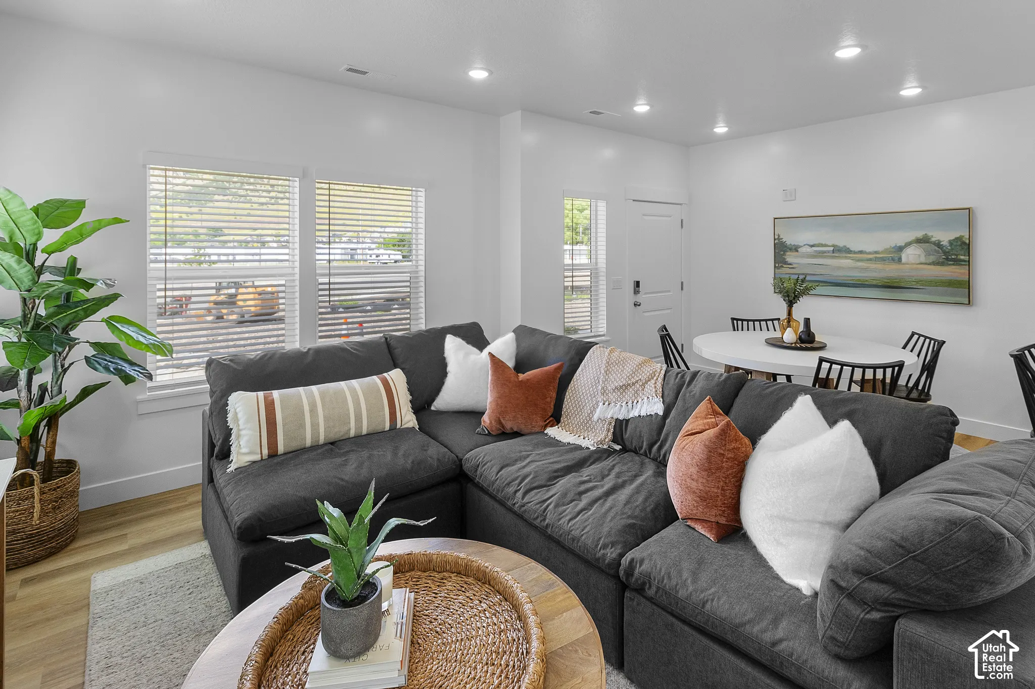 Open-concept living area featuring wood-finish flooring, white walls, recessed lighting, and multiple windows with blinds