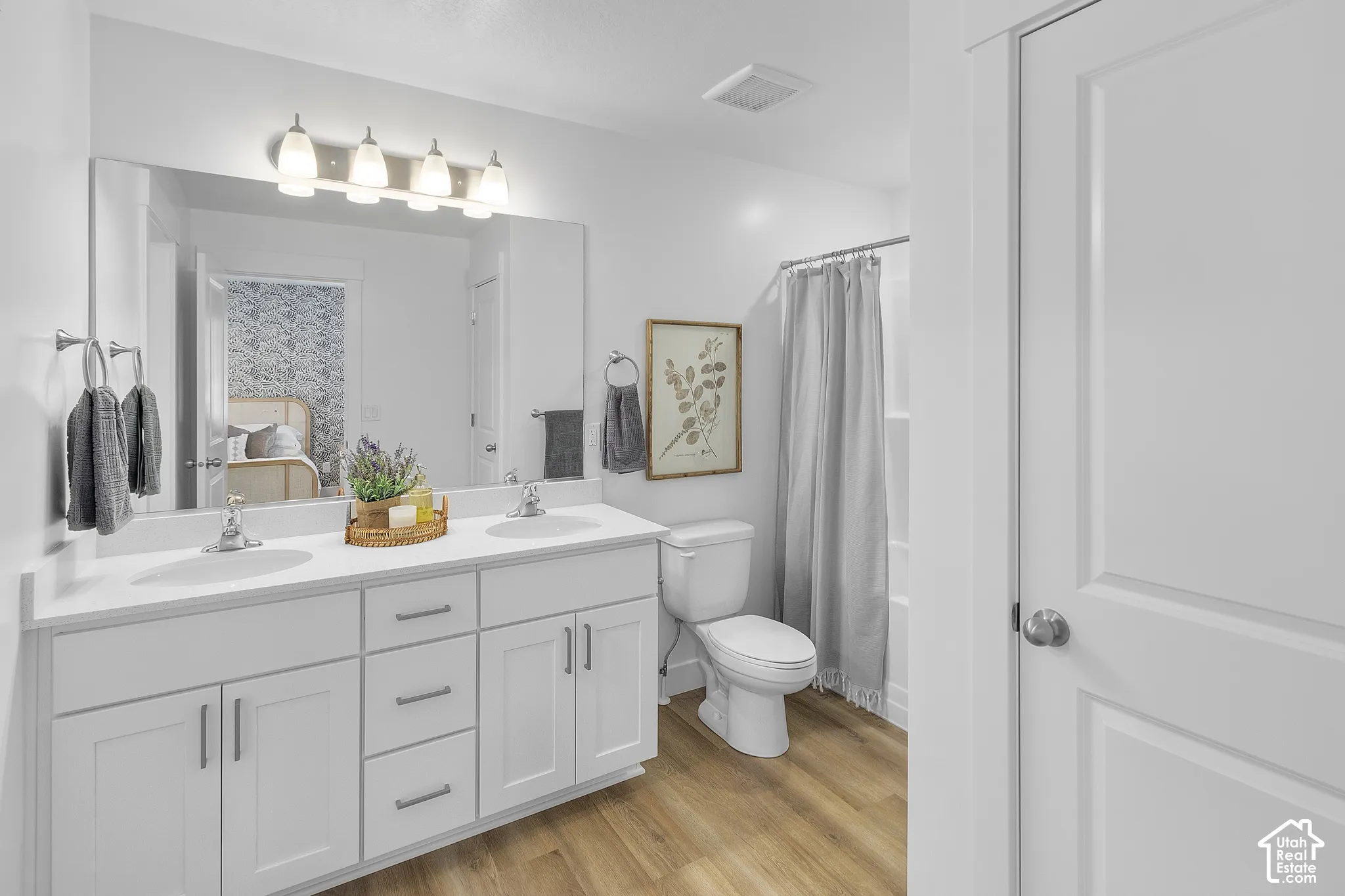Dual vanity with white cabinetry and integrated sinks, wood-finish flooring, and a shower-tub combination with a curtain rod