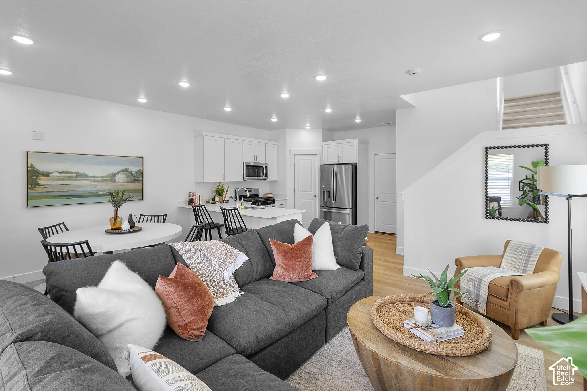 Open-concept living area featuring a kitchen with white cabinetry and stainless steel appliances, a dining area with a round table, and wood-finish flooring