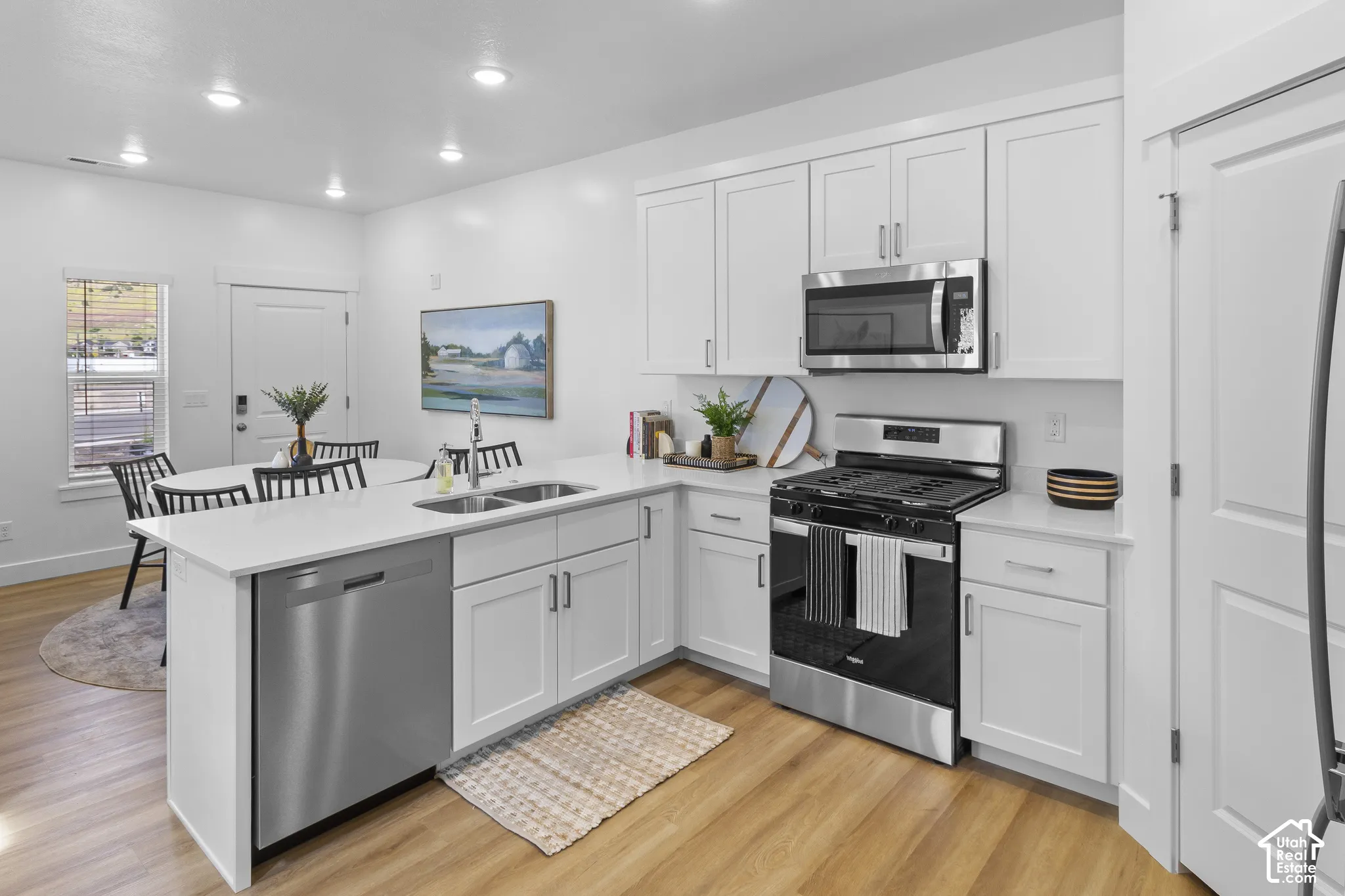 Kitchen featuring white cabinetry, stainless steel appliances, wood-finish flooring, recessed lighting, and a white countertop