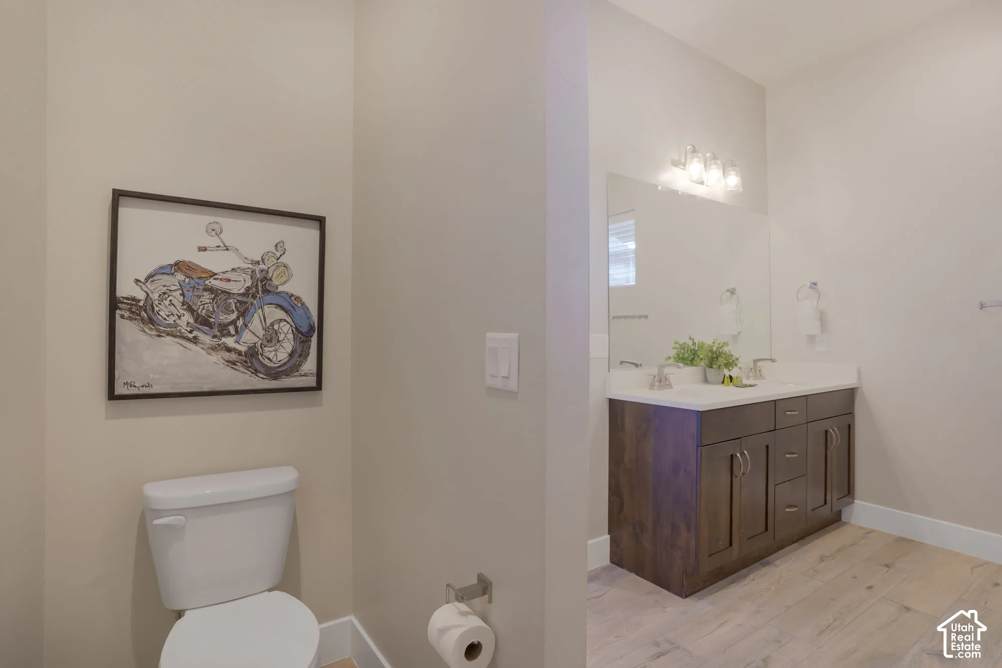 Dual vanity with integrated sinks, wood-finish cabinetry, a large mirror, and light wood-finish flooring