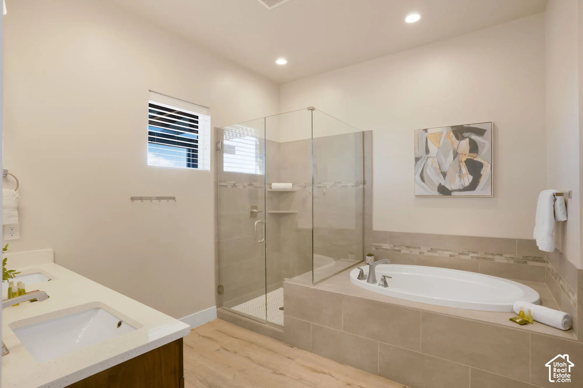 Dual vanity with undermount sinks and quartz countertops, glass-enclosed shower with tile surround, built-in soaking tub with tile surround, recessed lighting, and wood-finish flooring
