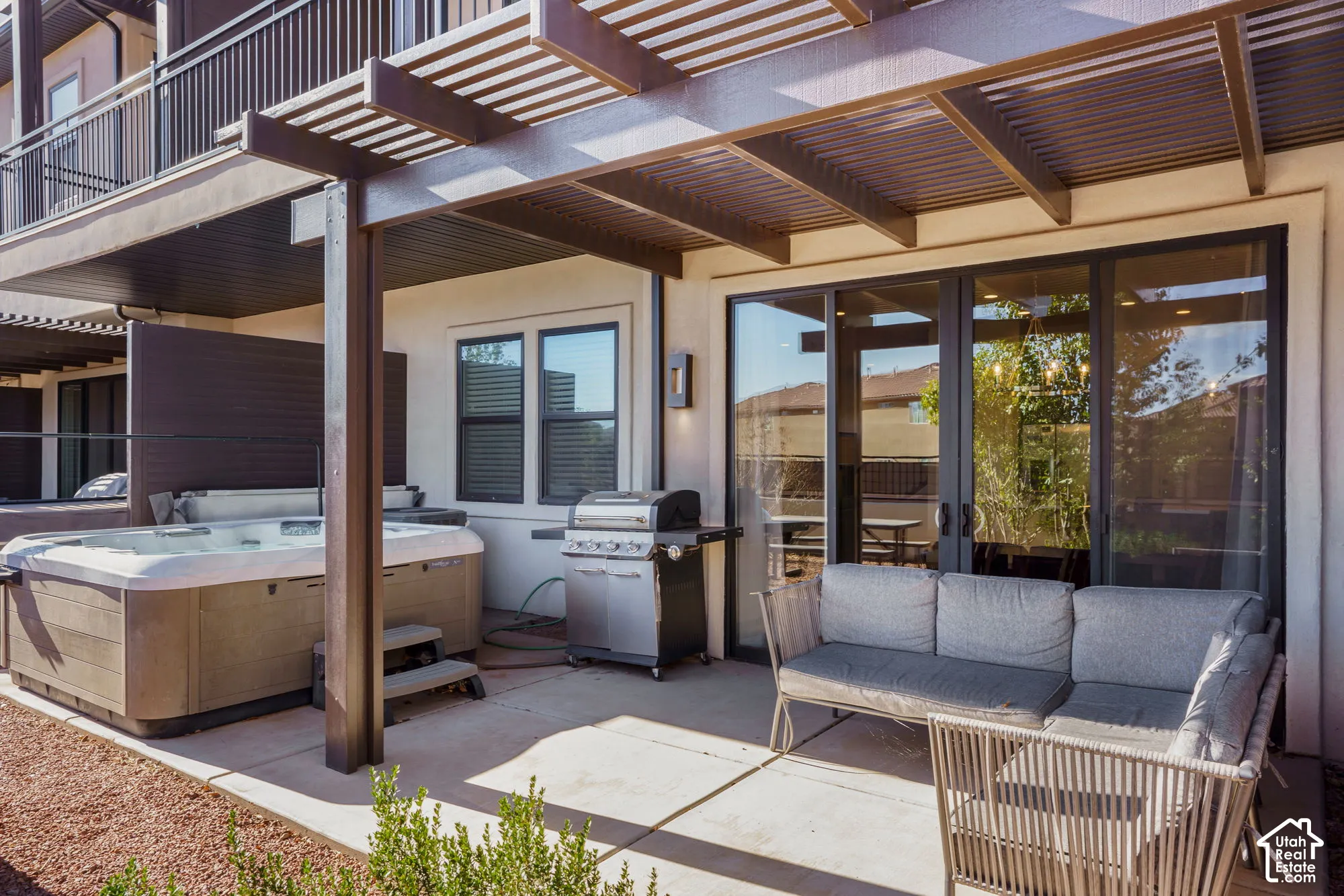 Paved patio featuring an integrated hot tub, privacy screening, a slatted pergola, and large sliding glass doors
