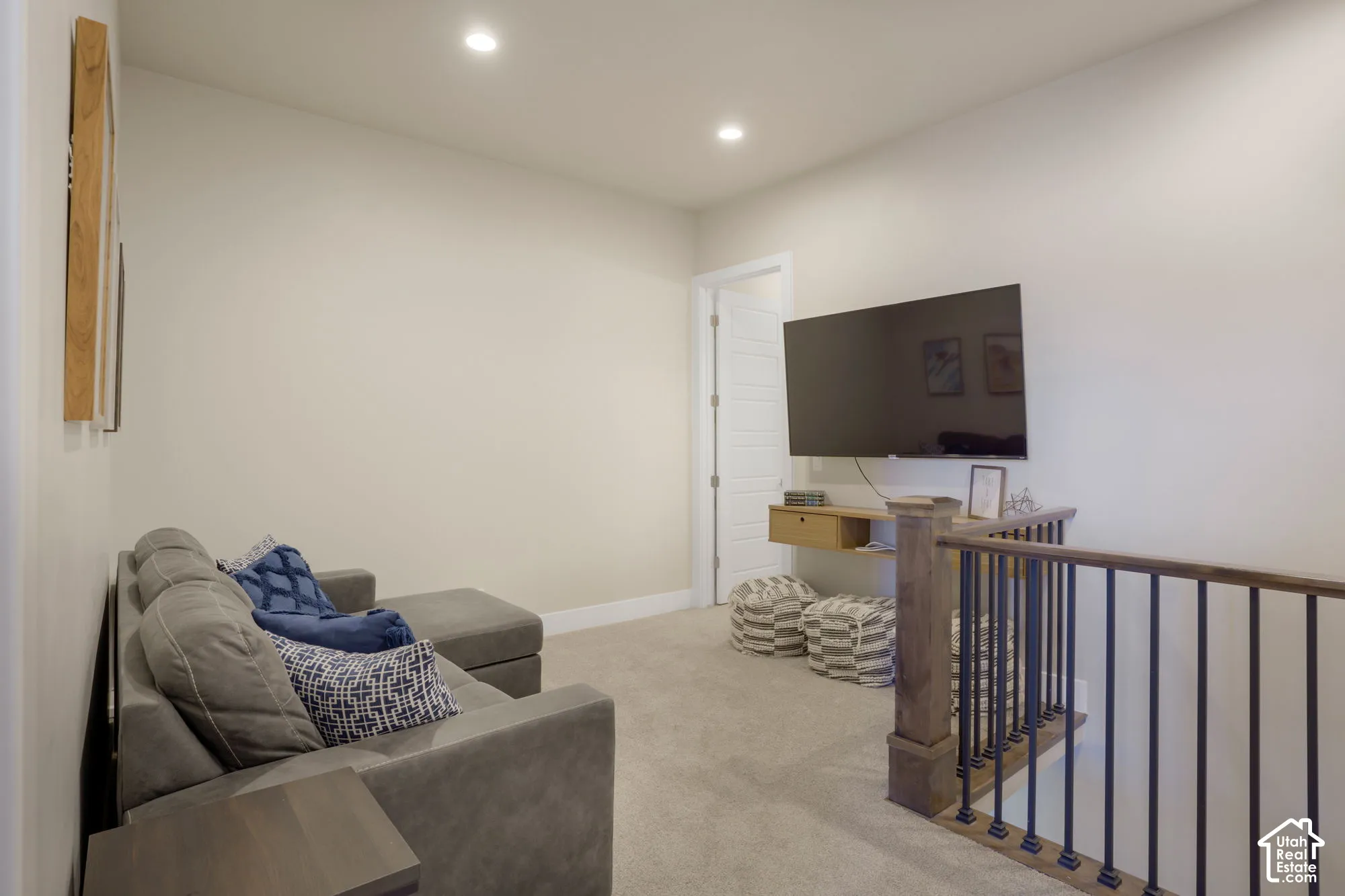 Recessed ceiling lighting, light-colored carpeting, white walls, and a wood and iron railing