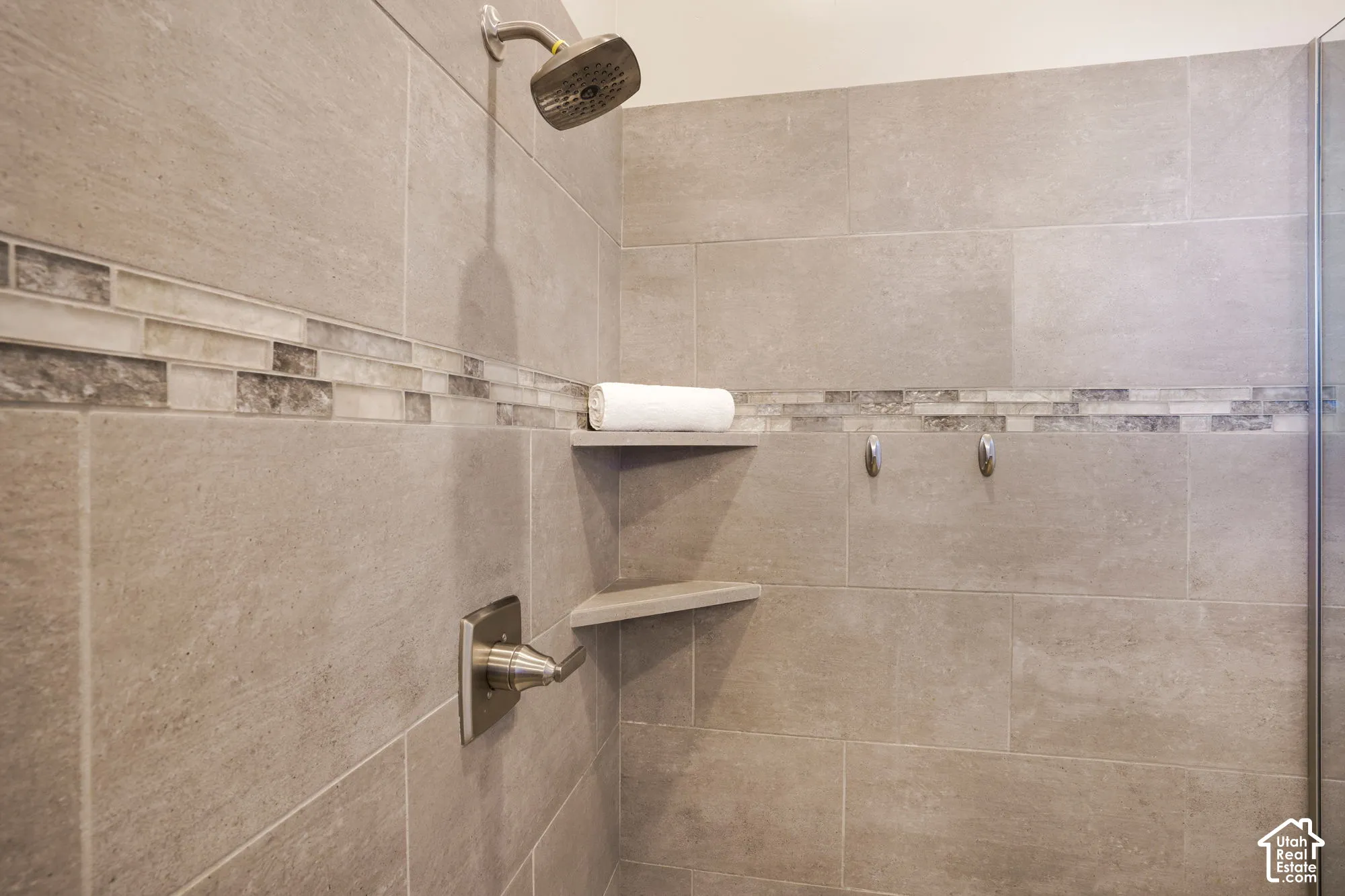 Tile shower surround with an accent mosaic band, built-in corner shelves, and a brushed nickel shower head