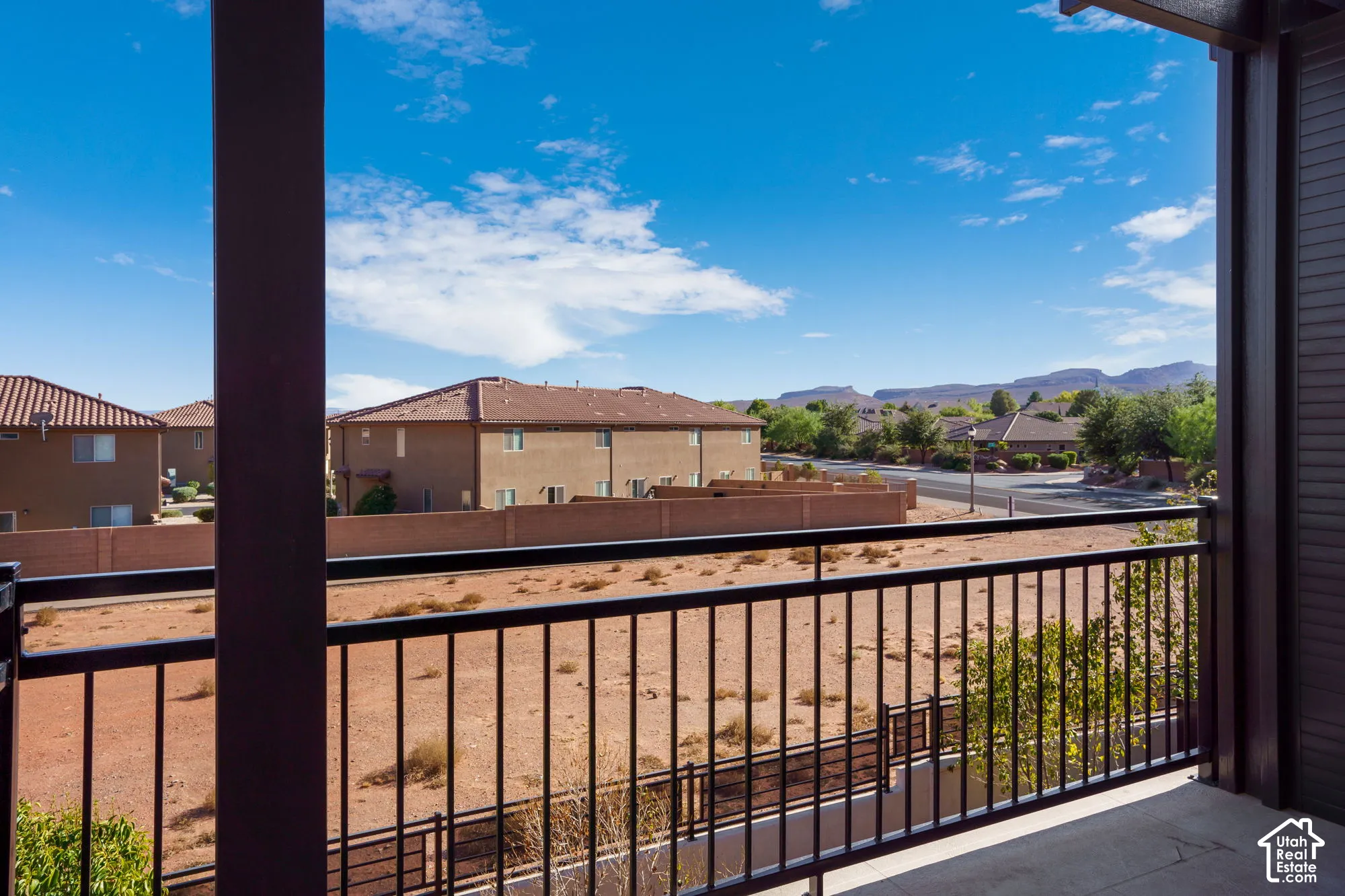 Balcony with black metal railing overlooking a residential area with tile-roofed structures and distant mountains