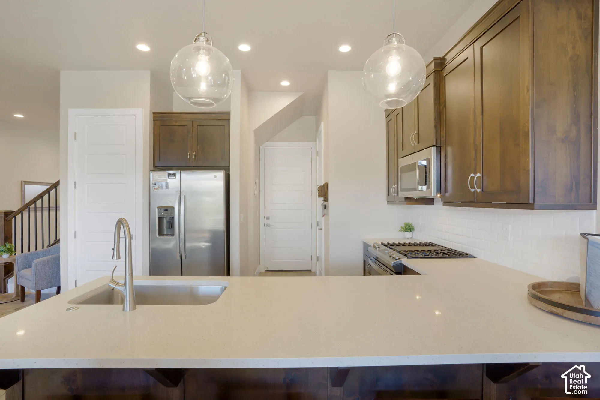 Kitchen featuring a peninsula with a built-in sink, stainless steel appliances, dark wood-finish cabinetry, and recessed lighting