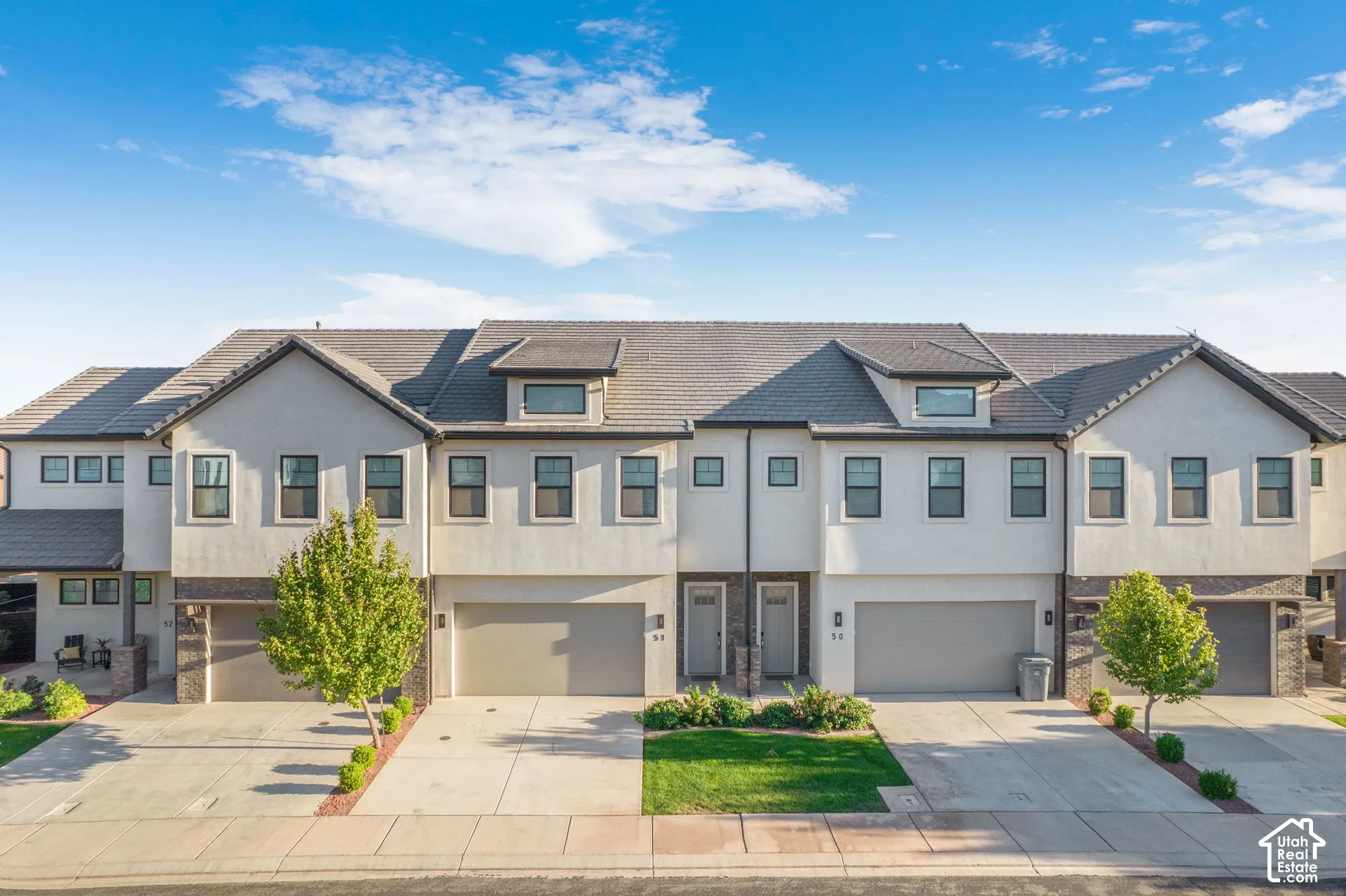 Contemporary townhome exteriors featuring light stucco, dark-framed windows, and integrated garages