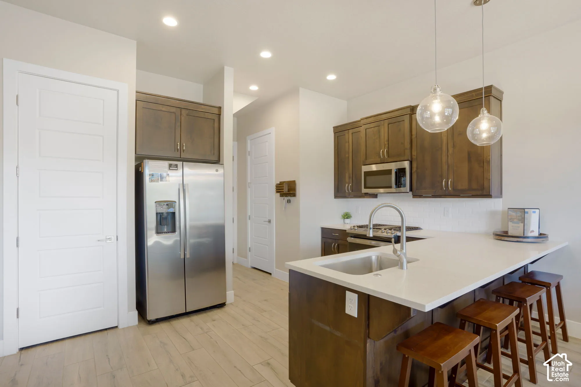 Kitchen featuring wood-finish cabinetry, stainless steel appliances, a white countertop island with an undermount sink, and recessed lighting