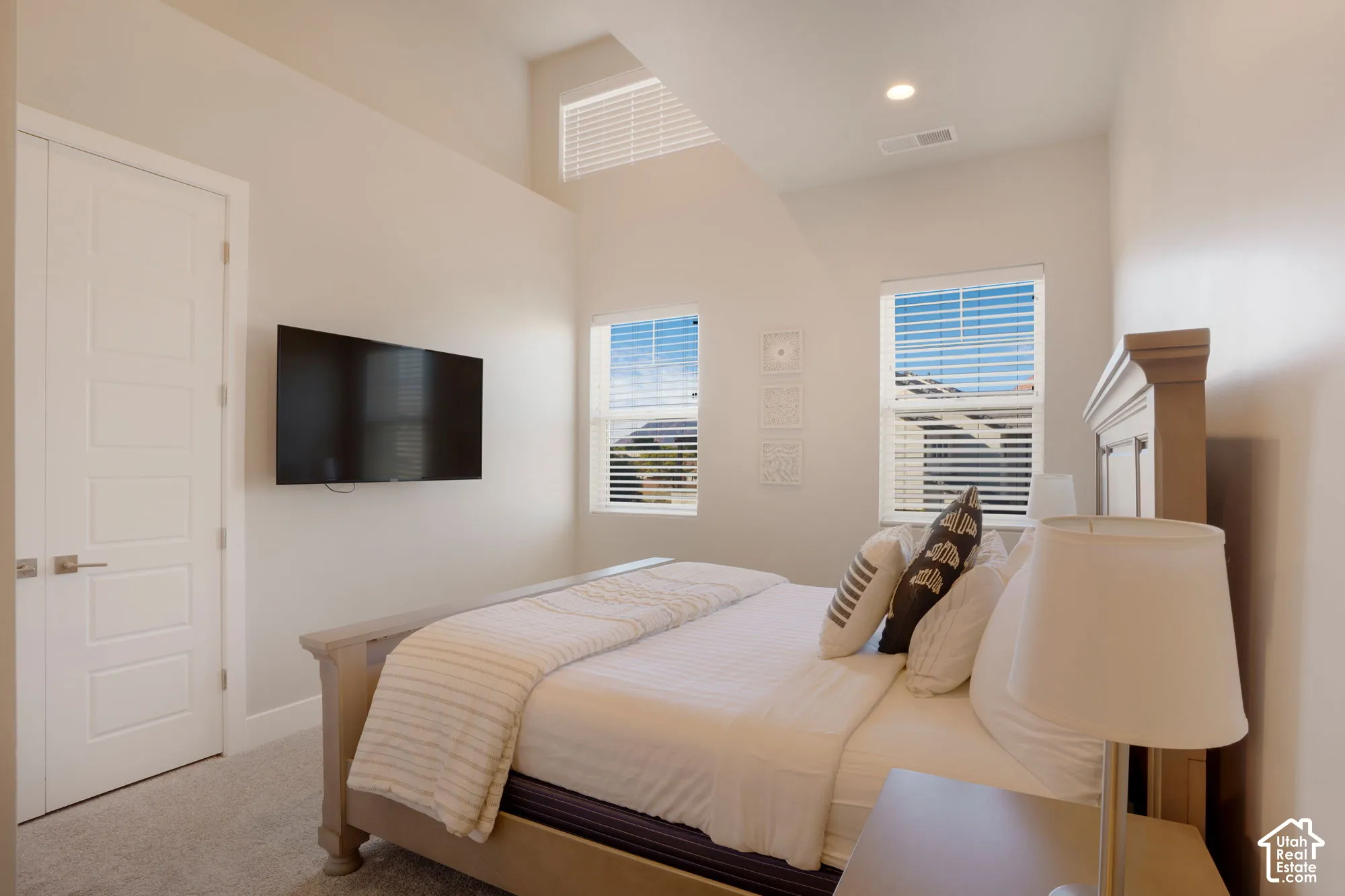 Vaulted ceilings featuring an upper transom window, two double-hung windows with blinds, recessed lighting, and soft gray carpeting