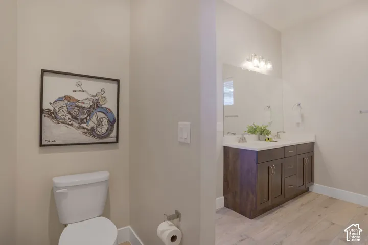 Dual vanity with integrated sinks, wood-finish cabinetry, a large mirror, and light wood-finish flooring