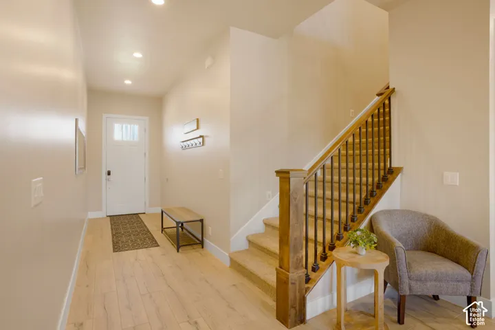 Entryway featuring wood-finish flooring, recessed lighting, a staircase with carpeted treads, and a wood newel post with metal balusters