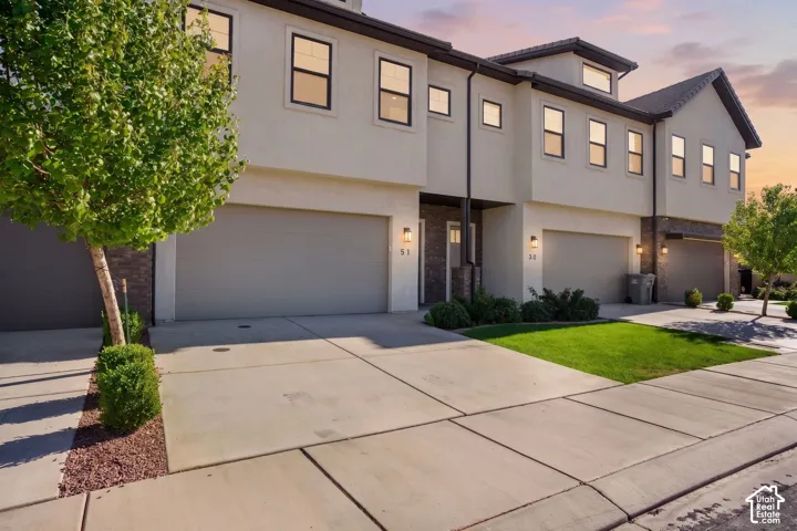 Contemporary townhome exterior with smooth stucco facade, dark-framed windows, integrated garage doors, and structured landscaping