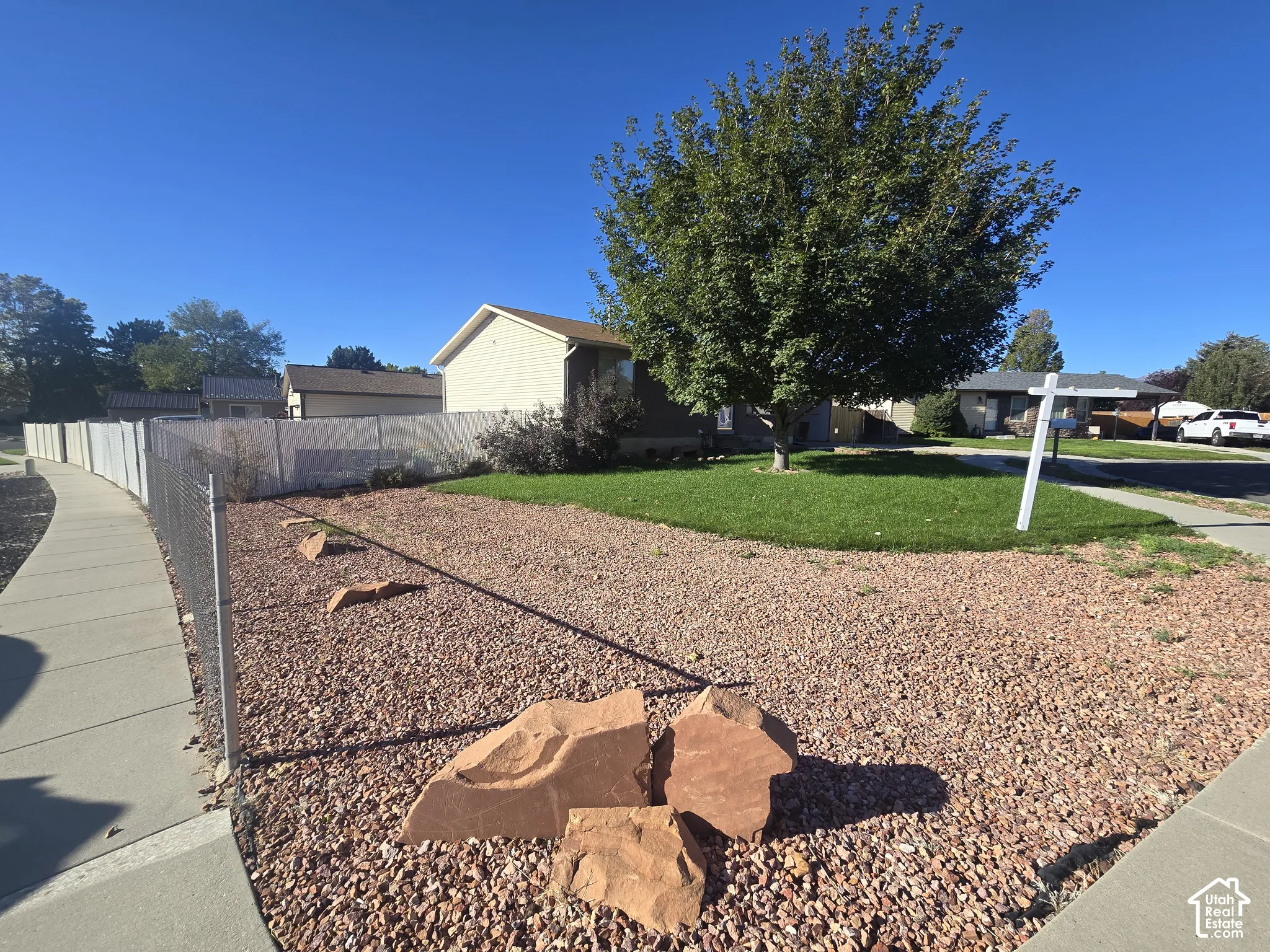 Xeriscaped front yard with decorative rocks, mature tree, and a concrete sidewalk