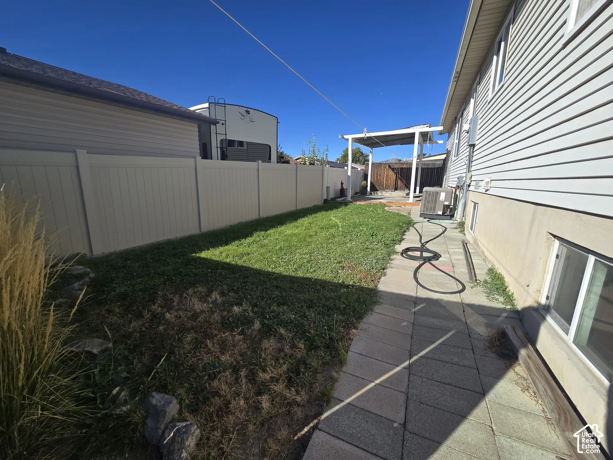 Expansive backyard featuring a manicured lawn, full-height privacy fencing, a paved pathway, and a covered patio structure