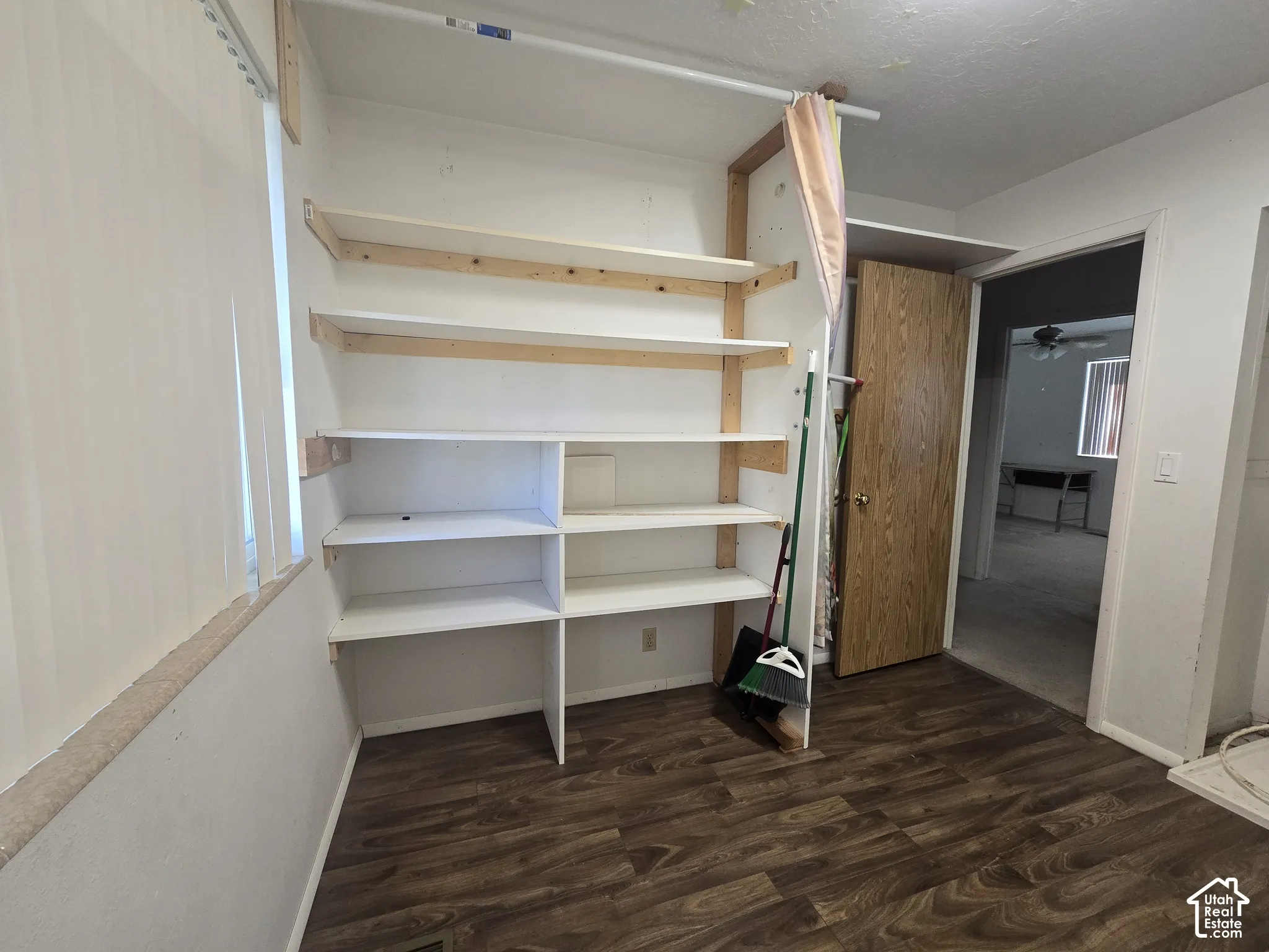 Wood-finish flooring, built-in shelving, and a window with vertical blinds