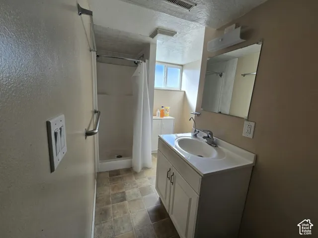 Tile-finish flooring, single-sink vanity with white cabinetry, wall-mounted mirror, and a shower stall with a grab bar