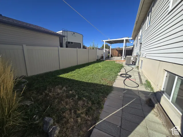 Private backyard with a covered patio, manicured lawn, and block paver pathway