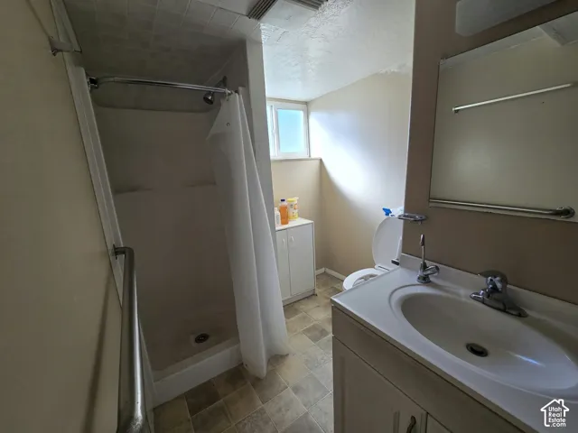 Bathroom featuring a shower stall with a grab bar, a single vanity with a white sink, a wall-mounted mirror, and a small built-in cabinet