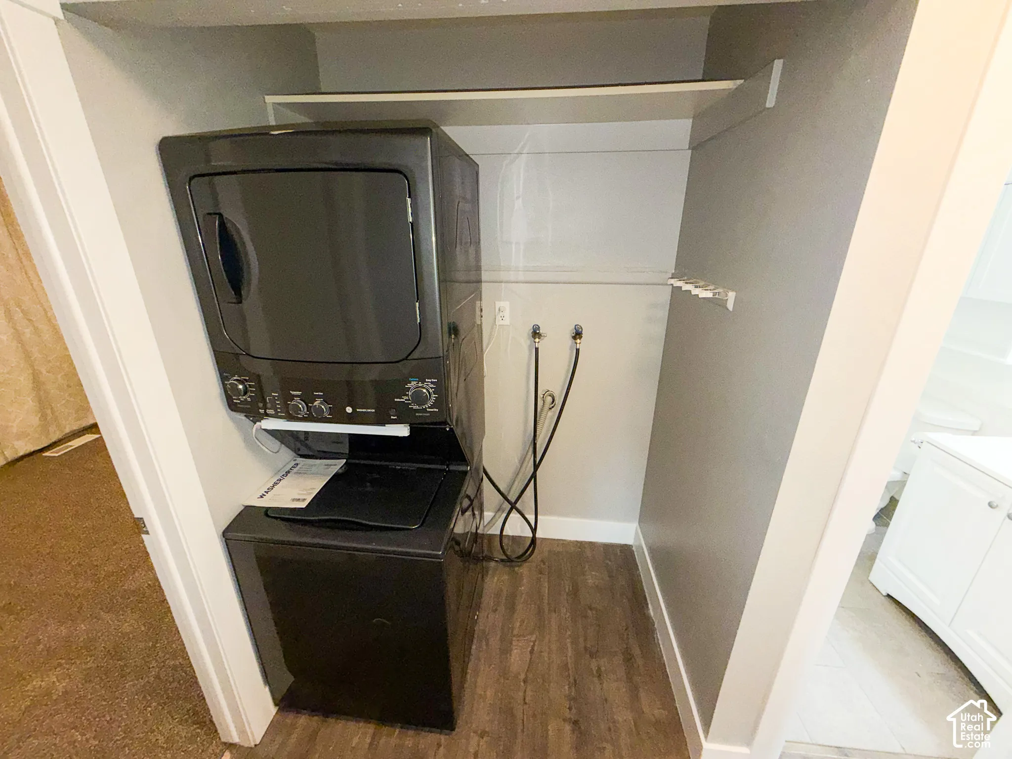 Compact laundry area featuring a stacked washer and dryer, wood-finish flooring, and built-in shelving