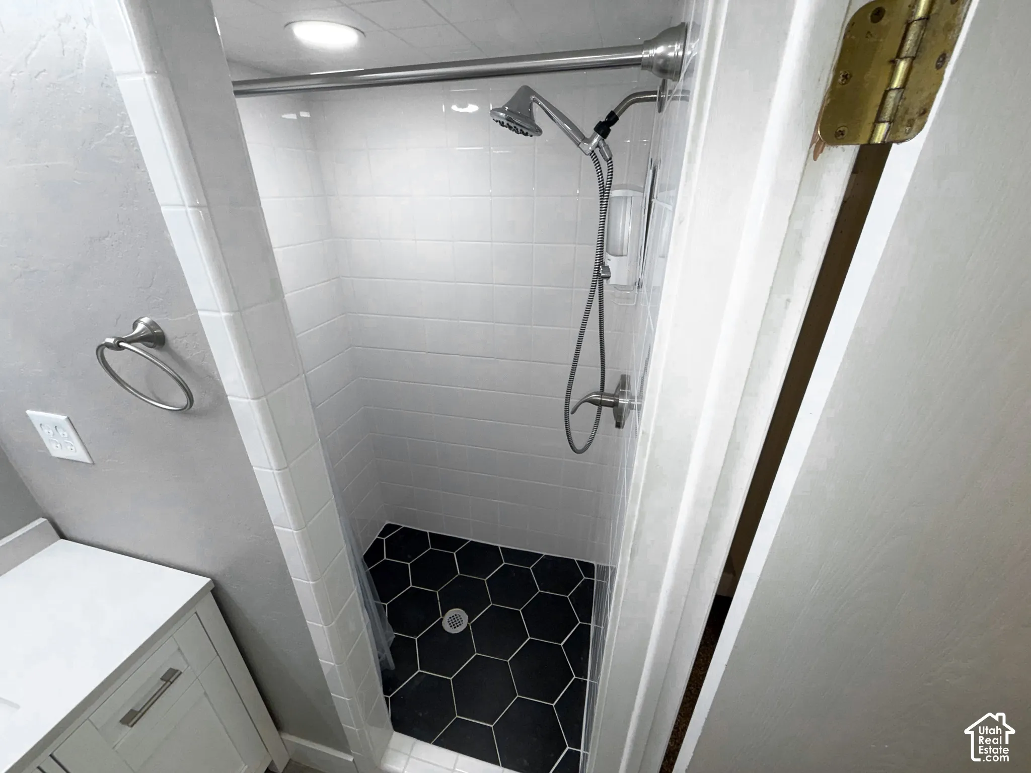 Shower stall with white subway tile walls, black hexagonal floor tile, and a chrome shower head with a handheld sprayer