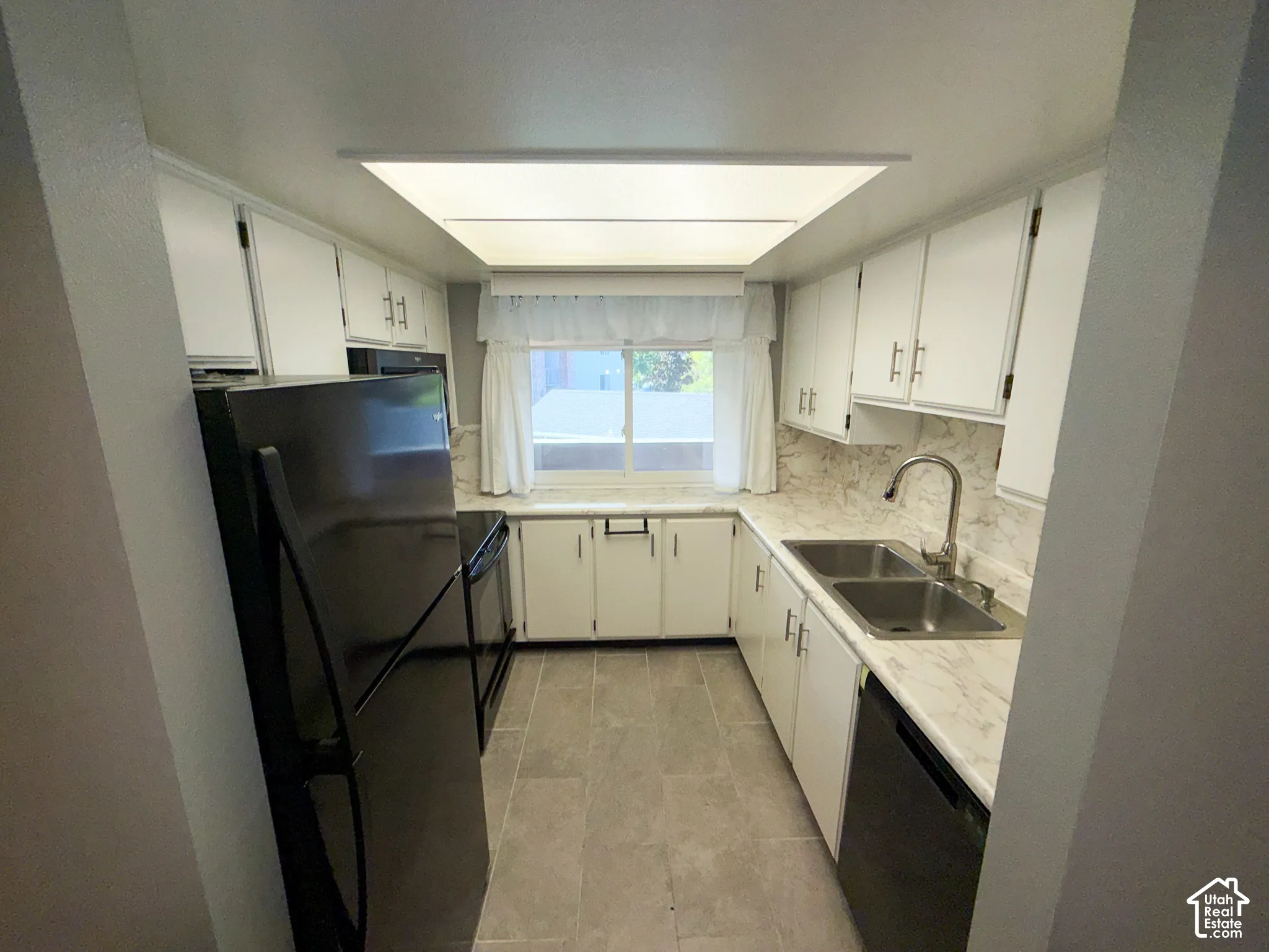 Galley kitchen featuring white cabinetry, light countertops, and a dual basin stainless steel sink