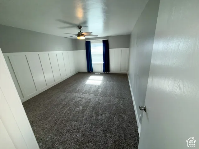 Textured gray carpeting, a ceiling fan with integrated lighting, and a white paneled accent wall