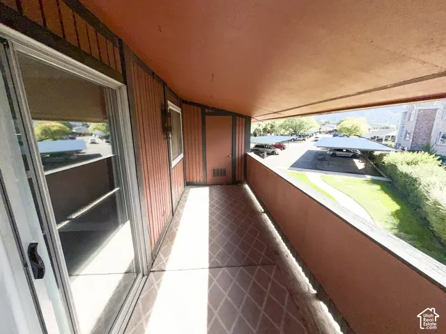 Outdoor covered balcony with a sliding glass door, patterned floor tiles, and wood-paneled siding