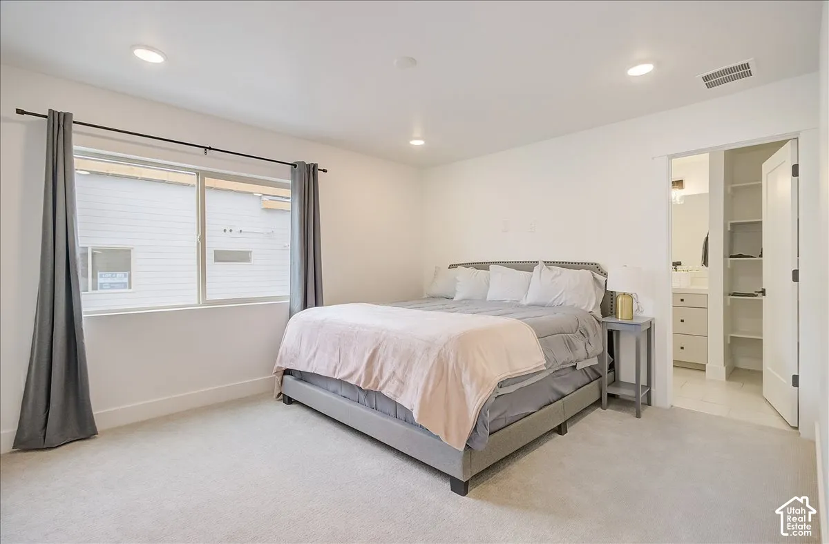 Recessed lighting, large window with expansive sill, carpeted flooring, open doorway to an adjoining bathroom, and a built-in shelving unit