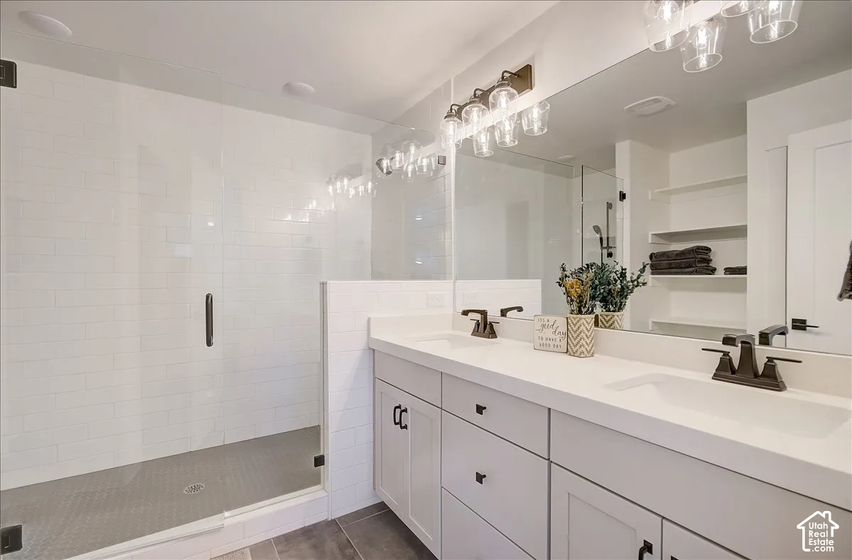 Dual vanity with white cabinetry and integrated sinks, a large frameless mirror, and a glass-enclosed shower with subway tile surround and mosaic tile floor