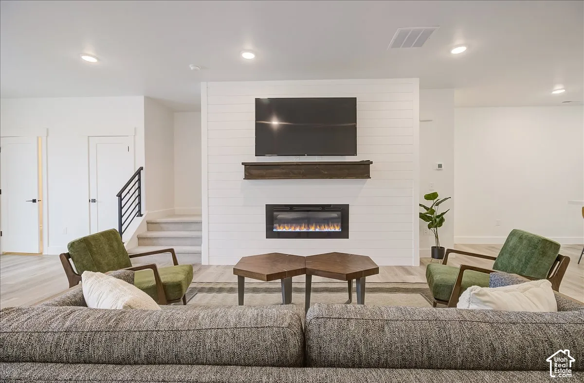 Living area with shiplap feature wall, integrated electric fireplace, and wood-finish flooring