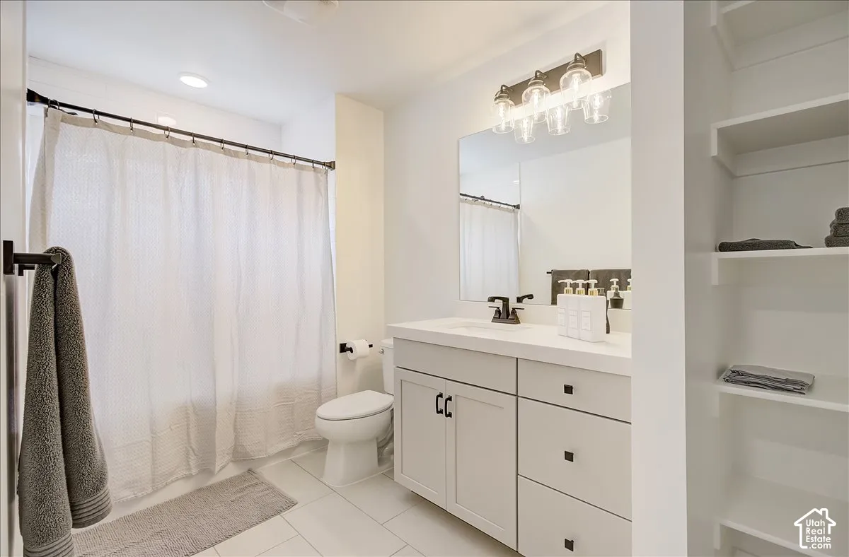 White tile flooring, recessed ceiling lighting, a vanity with a white countertop, dark-finish hardware, and built-in shelving