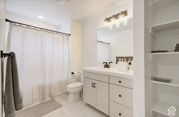 White tile flooring, recessed ceiling lighting, a vanity with a white countertop, dark-finish hardware, and built-in shelving