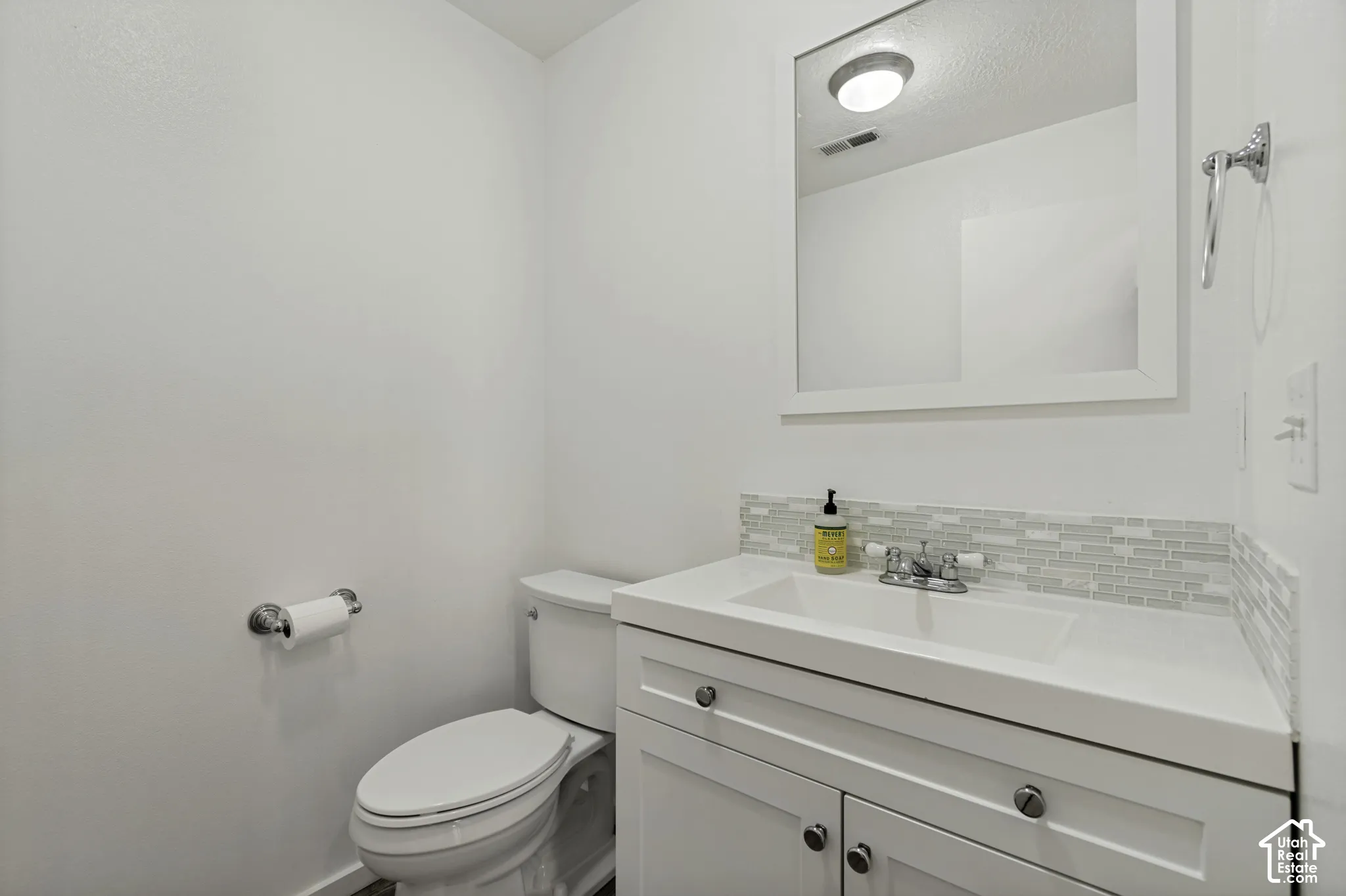 White vanity with chrome hardware, integrated sink, and mosaic tile backsplash