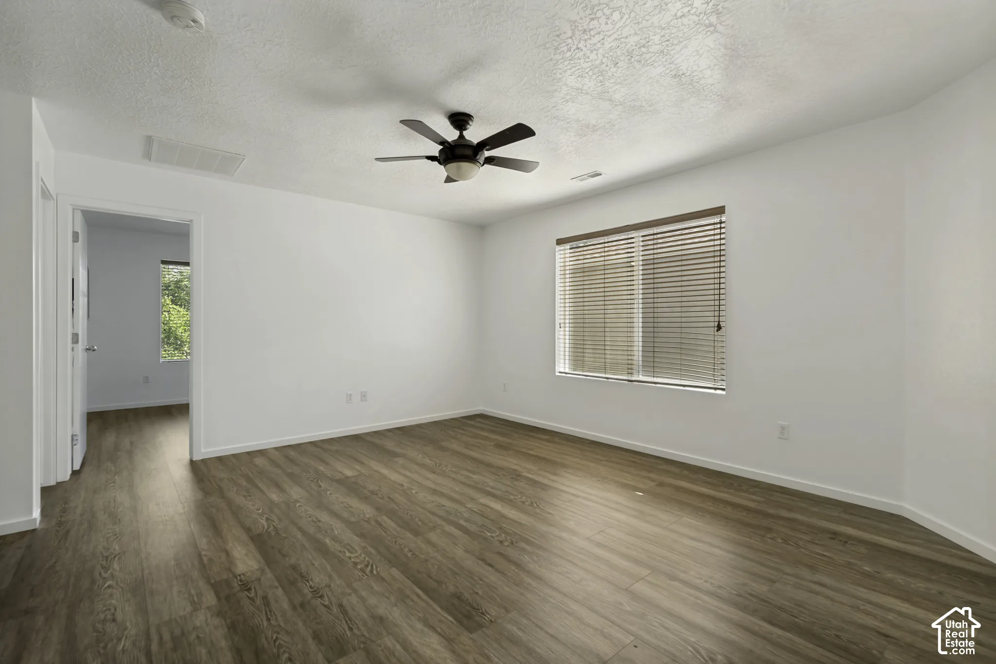Expansive room featuring wood-finish flooring, a ceiling fan, and a large window with blinds