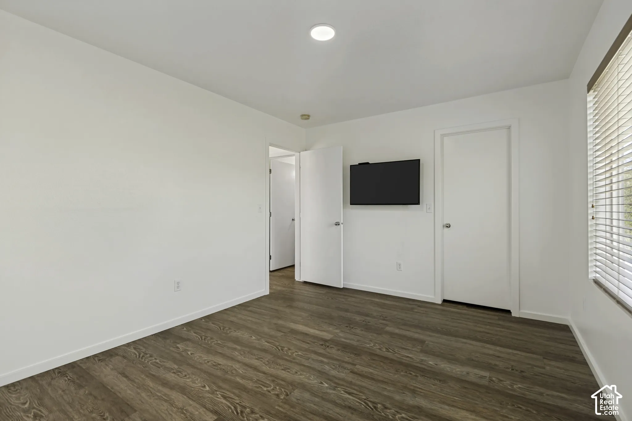 Wood-finish flooring, white walls, and a window with blinds
