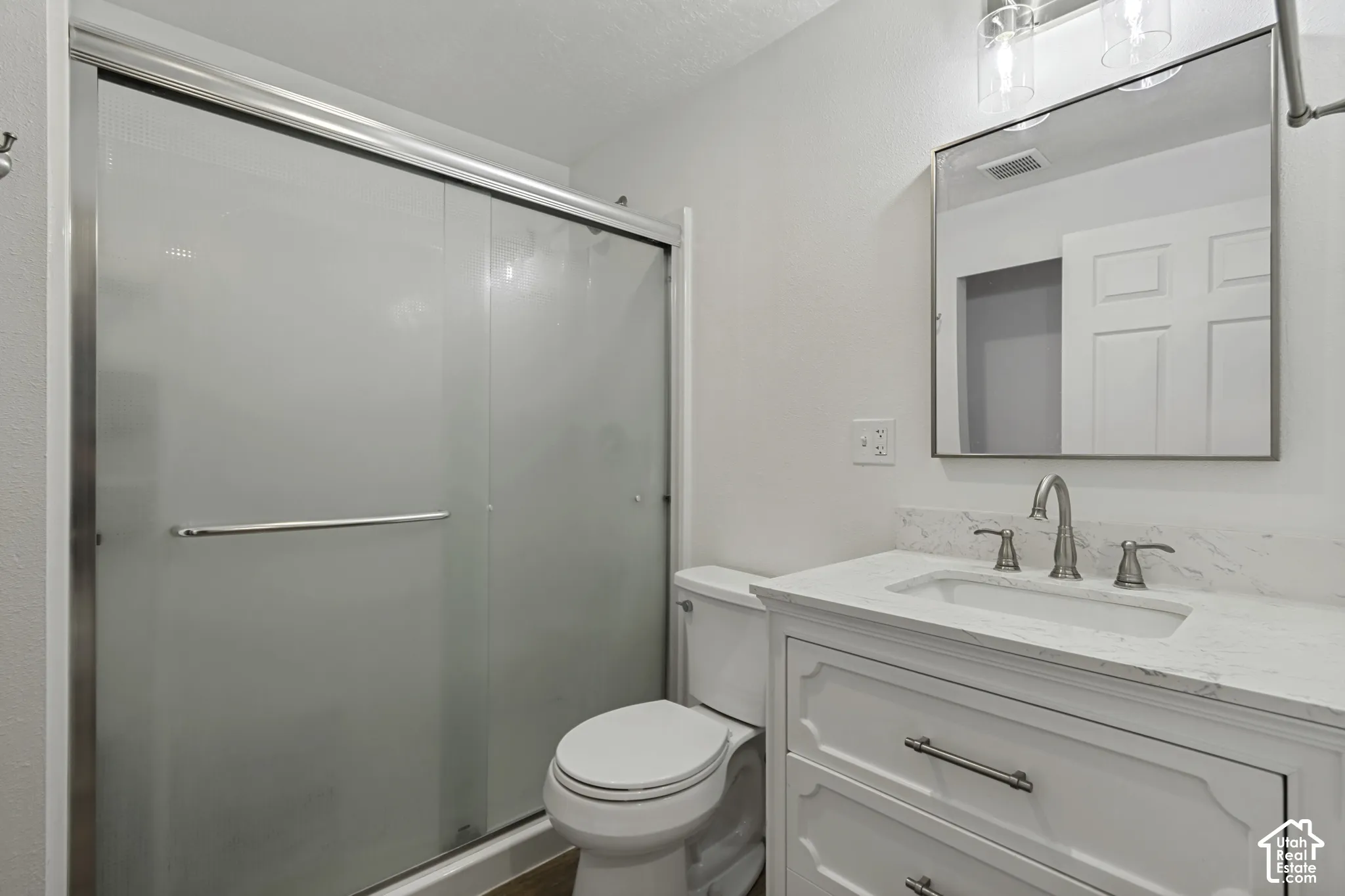White vanity with drawer storage, rectangular undermount sink, brushed nickel faucet, framed mirror, and a shower with frosted sliding glass doors